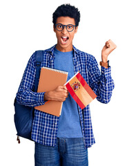Young african american man wearing student backpack holding spanish flag screaming proud,...