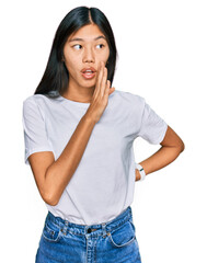 Beautiful young asian woman wearing casual white t shirt hand on mouth telling secret rumor, whispering malicious talk conversation