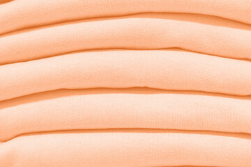 Stack of woolen sweaters in trending color of year 2024 Peach Fuzz.