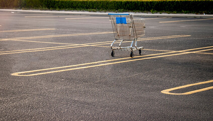  A Lone shopping cart in an empty parking lot  in afternoon light - obrazy, fototapety, plakaty