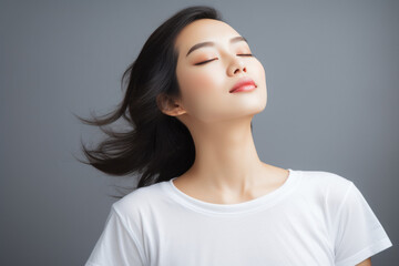 Beautiful young Asian woman wearing a white t-shirt Close your eyes and feel happy and relaxed. Isolated empty space on a gray background.
