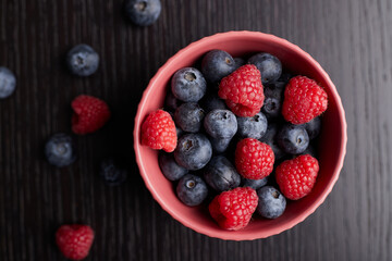 Top view, close-up of raspberries and blueberry in a bowl on wood table background.