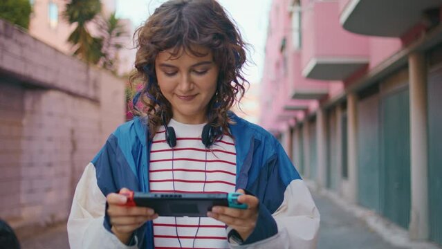 Teenager playing handheld console walking urban area. Woman focused on display 