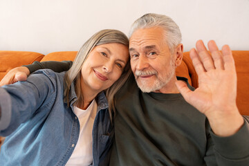 Happy elderly couple smiling on sofa, embracing and looking at camera. Couple taking a selfie....