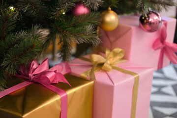 Obraz na płótnie Canvas Big Wrapped Gift Boxes Is Under the Christmas Tree. Pink and Gold Gift-Wrapped Box with Ribbon for Friends, Relatives. Close up. Packaging of Xmas Presents. Festive Decorations. Preparing for Holidays