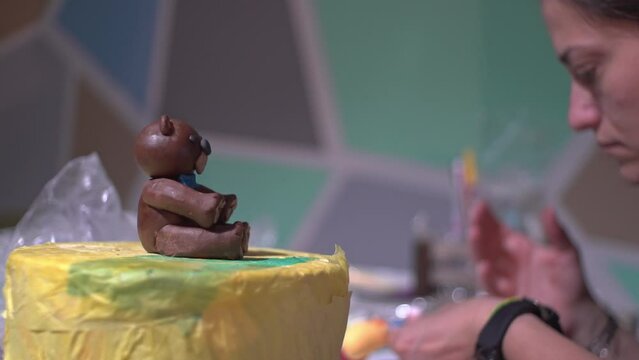 Side view of caucasian woman decorating a cake with sugar paste fondant bear at home. 4K shallow depth of field pan shot