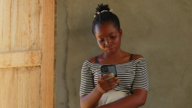 black young millennial female woman chatting with her smartphone sitting in remote african village