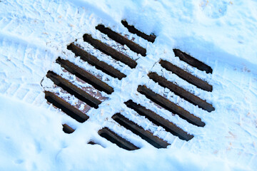 The sewer is covered with snow in winter. The drain grate is closed. Danger of falling into a hatch.