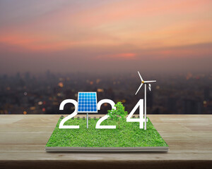 2024 white text with solar cell, wind turbine and growing tree on green grass on open book on...