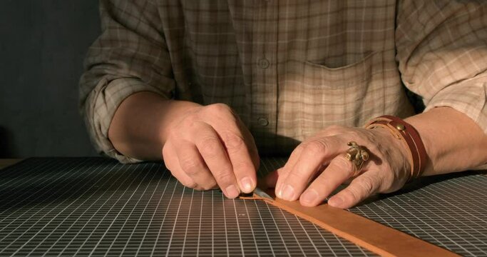 mature man hands sharpening Leather Edge Beveller before cutting the edge of handmade leather belt. Slow motion side closeup cropped shot. Masterclass, workshop session.