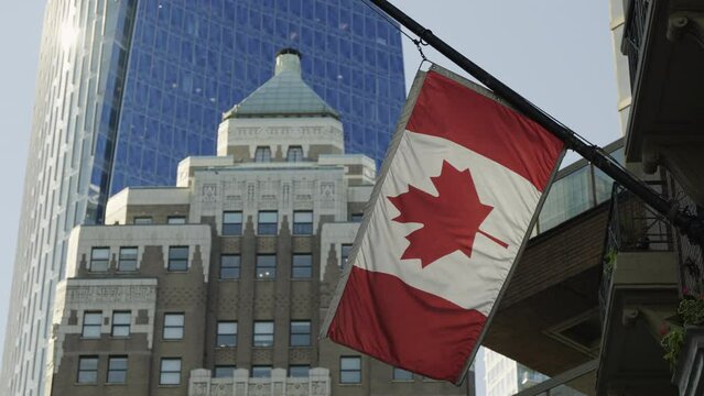 Canadian flag hanging at house and waving in the wind in Downtown Vancouver, handheld static slow-motion.
