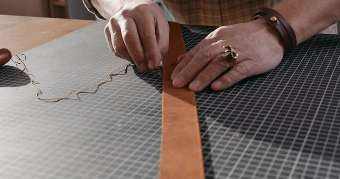 old mature craftsman smoothing edges of leather, artisan uses Leather edger at workplace, light room. male Cleaning Up the Edges of the Leather Belt Slow motion