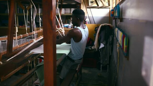 Man, floor treadle loom and weaving for production at clothing factory, manufacture and craftsmanship. Black male person, warehouse and thread or cotton industry, wool and fabric designer or textiles