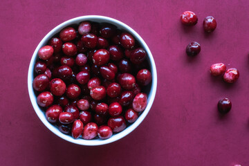 Overhead shot of cranberries in white bowl on red surface.