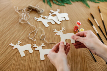 Hands crafting wooden reindeer ornaments on a table with paintbrushes