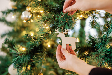 Hands placing wooden reindeer ornament on lit tree