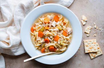Close up of chicken noodle soup in white bowl on beige background.