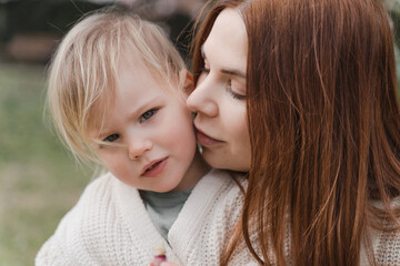 A woman kiss her little daughter near a blooming magnolia tree.