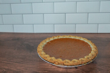 Pumpkin pie on a wood countertop and white tile background