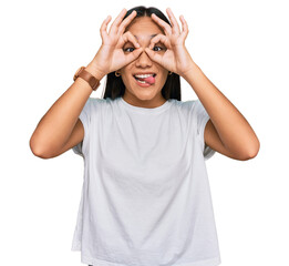 Obraz na płótnie Canvas Young asian woman wearing casual white t shirt doing ok gesture like binoculars sticking tongue out, eyes looking through fingers. crazy expression.