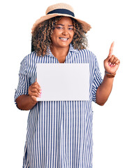 Young african american plus size woman holding cardboard banner with blank space surprised with an...