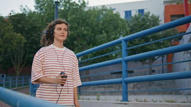 Pretty girl walking earphones at urban summer weekend. Woman moving in tact 