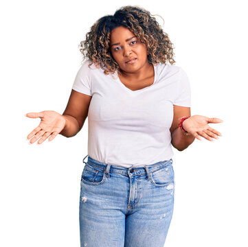 Young african american plus size woman wearing casual clothes clueless and confused expression with arms and hands raised. doubt concept.