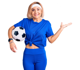 Young blonde woman holding soccer ball celebrating victory with happy smile and winner expression with raised hands