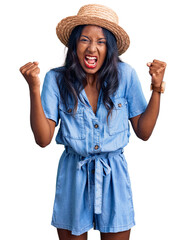 Young indian girl wearing summer hat angry and mad raising fists frustrated and furious while shouting with anger. rage and aggressive concept.