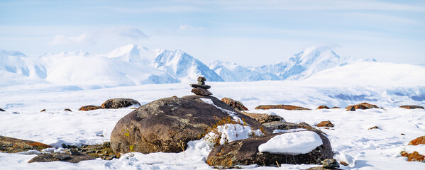 Cairn on a rock with the snow-covered Altai Mountains in the background under a clear sky.