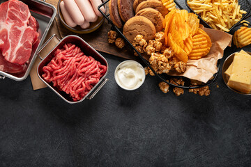 Saturated and trans. Unhealthy food. Sausage, potato, meat, cheese, popcorn, cookies, cream on dark background - obrazy, fototapety, plakaty