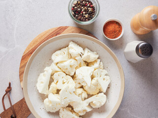 Close-up view of raw cauliflower florets on a plate ready for seasoning with paprika, salt and pepper. Food preparation.