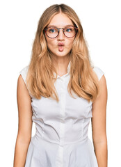 Beautiful young caucasian girl wearing casual clothes and glasses making fish face with lips, crazy and comical gesture. funny expression.