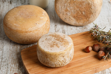 Artisanal and natural whole cheese, placed on a wooden board and without labels.
