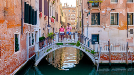 a couple of men and women on a city trip in Venice Italy sitting above a bridge at the canals of...