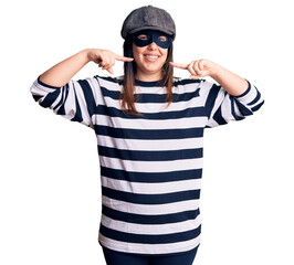 Young beautiful brunette woman wearing burglar mask smiling cheerful showing and pointing with fingers teeth and mouth. dental health concept.