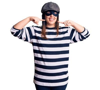 Young beautiful brunette woman wearing burglar mask smiling cheerful showing and pointing with fingers teeth and mouth. dental health concept.