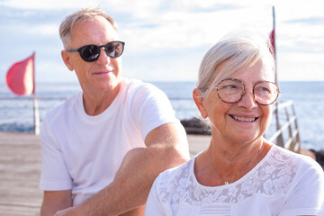 Senior woman and mature man friends sitting by the sea in sunset light, couple of people talking and stay together having fun enjoying freedom and vacation or retirement