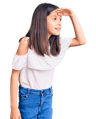 Beautiful child girl wearing casual clothes very happy and smiling looking far away with hand over head. searching concept.