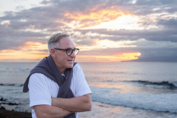 Portrait of senior mature man at the sea beach at sunset light looking the horizon over sea...