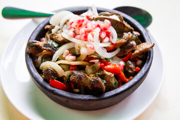 travel to Georgia - portion of Kuchmachi (Georgian dish of livers, hearts and gizzards with sliced fresh onion and pomegranate seeds for topping) in hot ceramic bowl on table close-up in local cafe