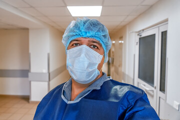 Portrait of a mature doctor in a protective mask and cap in the hospital corridor