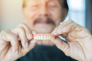 Grey haired senior man holding orthodontic prosthesis denture with a happy face standing and smiling