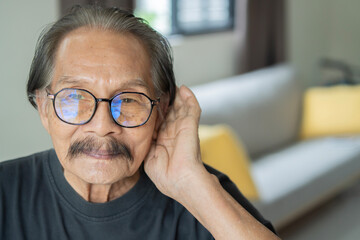 Senior Asian man, hard of hearing, placing hand on ear asking someone to speak up.