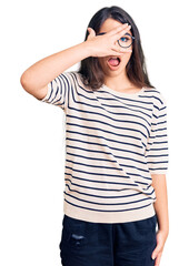 Fototapeta premium Brunette teenager girl wearing casual clothes and glasses peeking in shock covering face and eyes with hand, looking through fingers with embarrassed expression.