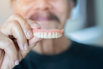 Waist up portrait of the old happy man in black t-shirt showing model of human teeth.