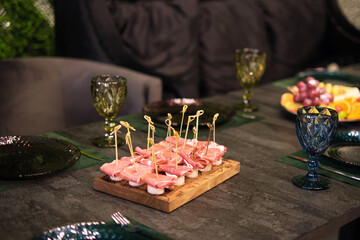 A wooden board with cured meats is the centerpiece in an elegant dining setting, paired with vintage green glassware. The setting speaks to a taste for gourmet experiences and entertaining.