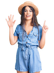Brunette teenager girl wearing summer hat showing and pointing up with fingers number six while...