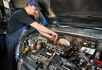 Side view of mechanic repairing car engine, working in garage, workshop, servicing center. Worker,...