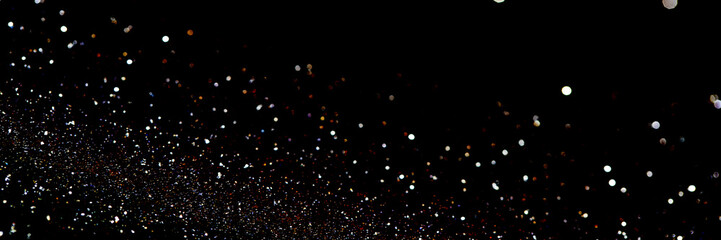 Glittering particles against a pitch-black background resembling a distant galaxy or the festive sprinkling of confetti in a dark night sky. Banner size